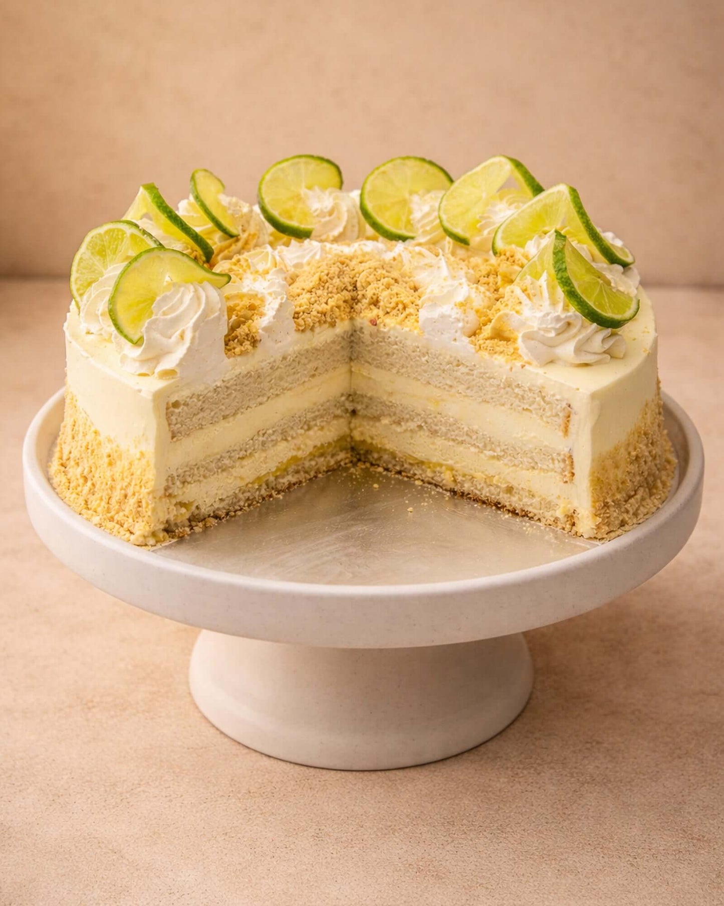 Lemon Gateau on a cake stand, featuring layers of vanilla sponge, fresh cream, and lemon cream filling, garnished with lime slices.
