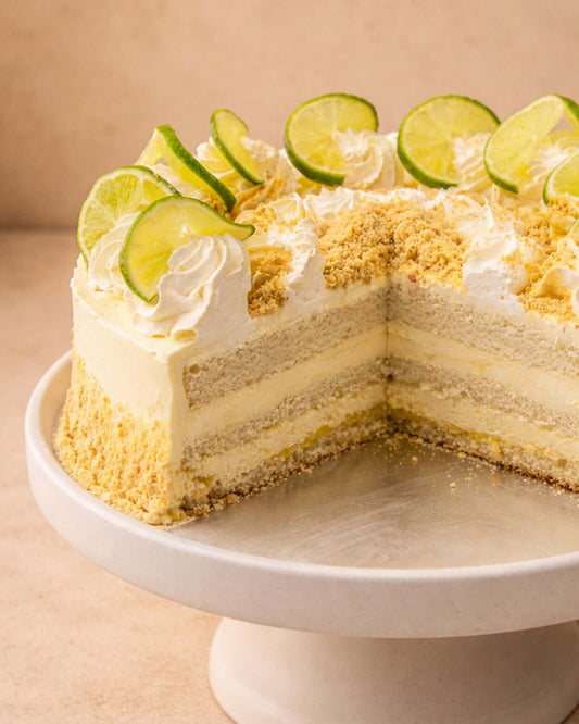 Lemon Gateau featuring layers of vanilla sponge, fresh cream, and lemon cream, topped with lemon slices and biscuit crumble.