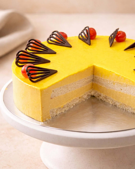 Mango mousse cake with chocolate decorations and cherry on top, showcasing a creamy, tropical dessert.