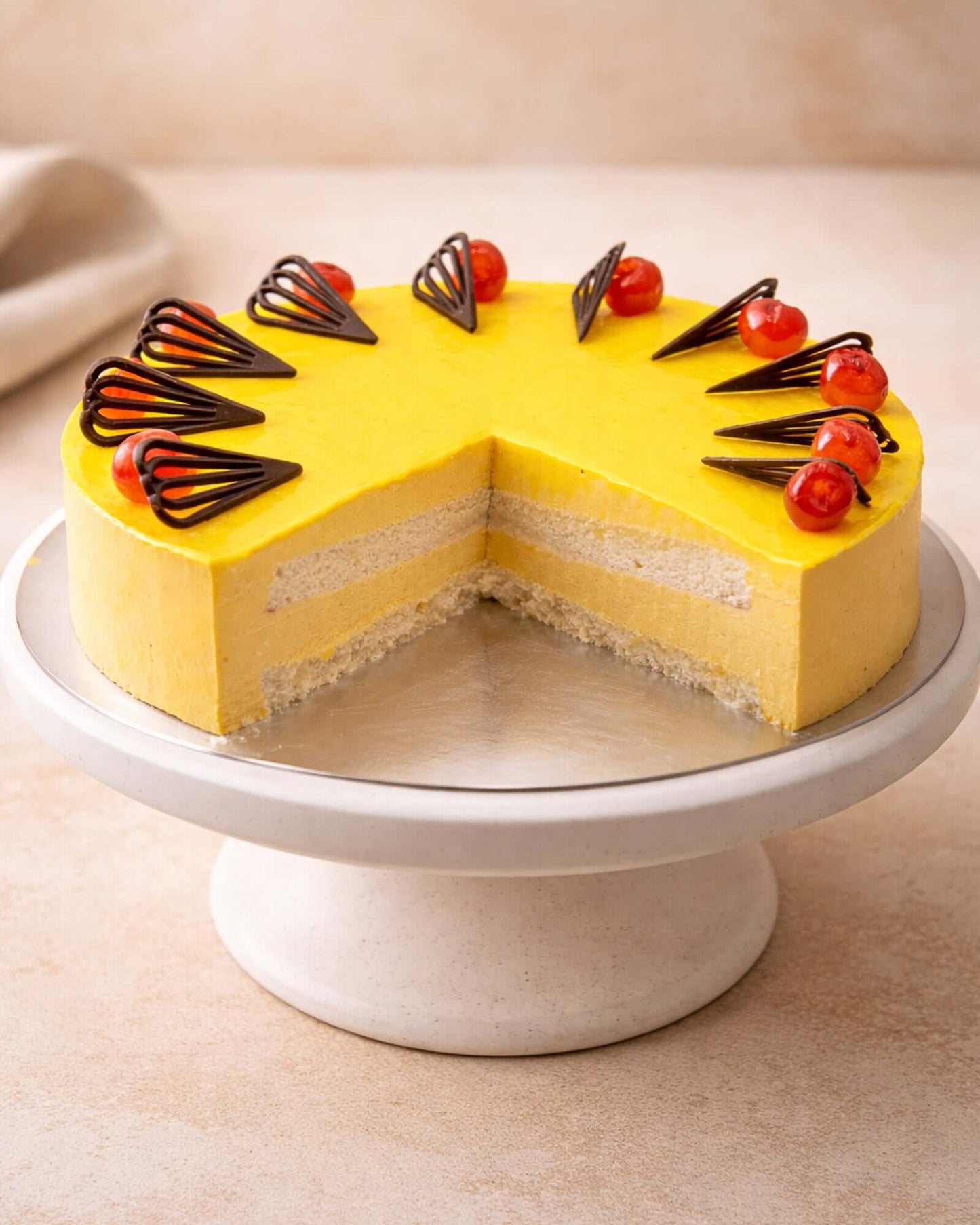 Mango mousse dessert with chocolate decoration and cherries on a cake stand, showcasing layers of light mousse.