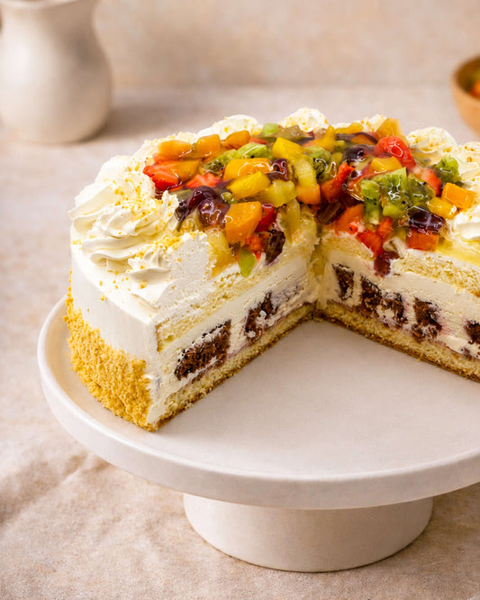 Mixed fruit gateau with layers of sponge, cream, and fresh fruits on top, displayed on a cake stand.