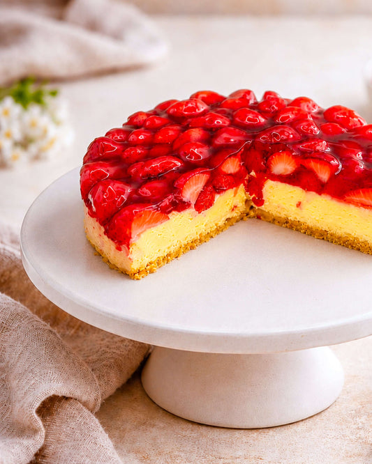 Strawberry Flan on a white cake stand, featuring a golden sponge base, fresh strawberries, and a glossy glaze.